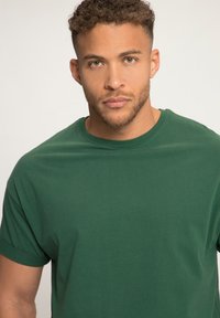 Camiseta de algodón verde con mangas cortas, presenta un cuello redondo y una textura suave y lisa. Diseño simple, sin patrones ni detalles.