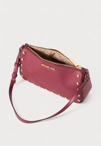 Pieni burgundinvärinen nahkainen Michael Kors -ranneke, jossa on kultaiset niitit ja vetoketju, näyttäen vaaleanbeigeä kangasvuoria, jossa on painettu logokuosi.