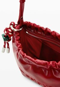 Geantă de mână din piele roșie cu închidere prin șnur, textură netedă și buzunar interior cu fermoar. Are o curea împletită și accente de hardware argintiu.