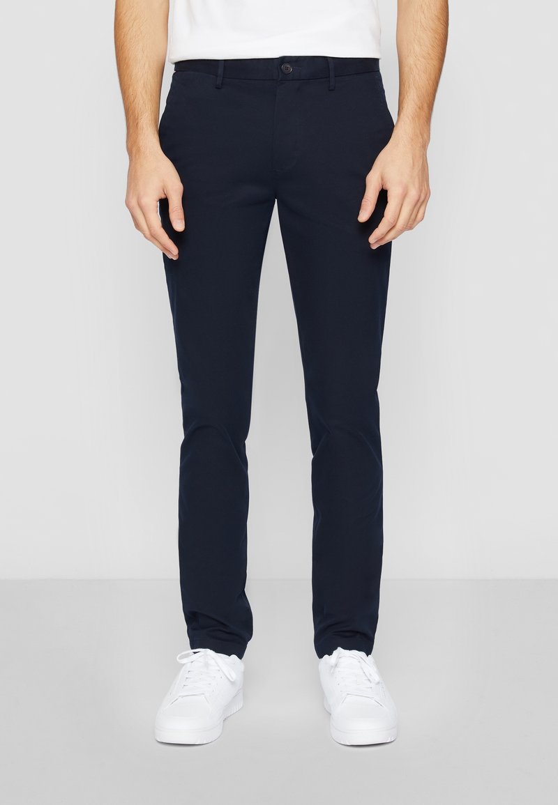 Granatowe chinosy wykonane z mieszanki bawełny, cechujące się slim fit, przednimi kieszeniami i zapięciem na guzik, w połączeniu z białymi sneakersami.