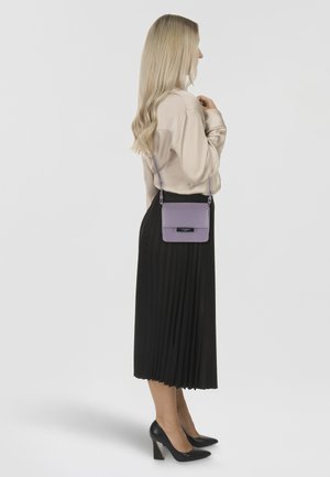 Lila Leder-Umhängetasche mit strukturiertem Design und silbernen Hardwareelementen, kombiniert mit einem langen schwarzen Plisseerock und schwarzen Absätzen.