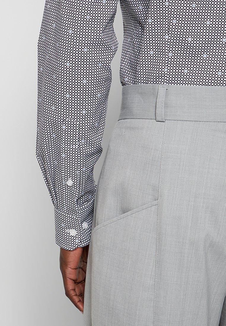 Camisa de manga larga con un patrón de lunares en blanco y negro, combinada con pantalones ajustados de color gris claro que cuentan con un bolsillo lateral y una textura suave.