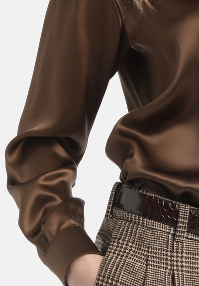 Bluză lungă din satin brown, cu mâneci lungi și croi lejer, cu mansete butonate, asortată cu pantaloni cu talie înaltă din țesătură cu pattern tartan și cu un curea lucioasă închisă la culoare.