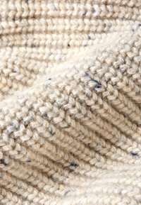 Strukturiertes beiges Gewebe mit einem Strickmuster und dezenten blauen Sprenkeln. Der Stoff wirkt weich und dick und betont ein geripptes Design.