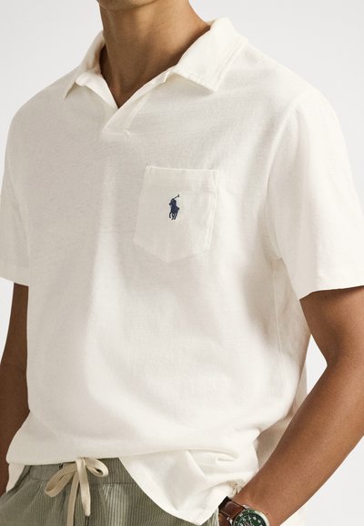 White polo shirt made of textured fabric, featuring a chest pocket with a dark blue logo. Short sleeves and a classic collar design.