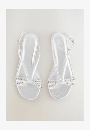 Silver strappy sandals featuring a glossy finish, clear straps, and rhinestone embellishments across the toe area and ankle strap.