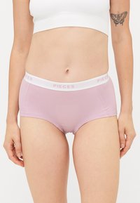 Lila pamutsztrumpa fehér derékrésszel, amelyen a "PIECES" márkaneve világos rózsaszínnel olvasható. Sima tapintású, kötött fazonú és hipster stílusú.