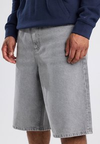 Shorts de mezclilla gris con un corte recto, que cuentan con un diseño de cinco bolsillos y dobladillos cosidos. La tela tiene una textura sutil y un aspecto desvanecido.