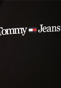 Sort bomuldsstof med teksten "Tommy Jeans" i hvidt og et lille rødt, hvidt og blåt logo mellem ordene.