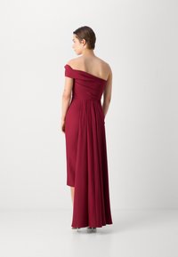 Rochie burgundy, cu umeri descoperiți, cu detalii din material drapat pe spate, până la genunchi, având un bust structurat și o textură fină.
