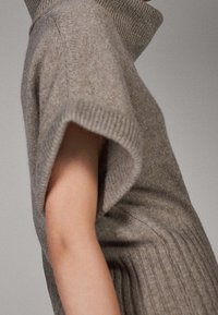 Harmaa neulepaita, jossa on korkeakauluksinen, resorikuvioitu kaulus ja lyhyet hihat, resorimainen rakenne ja sileä viimeistely, korostaen mukavuutta ja istuvuutta.