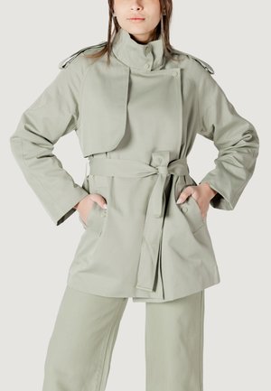 Cappotto trench verde chiaro con cintura, colletto alto e tasche laterali. Presenta una chiusura a bottoni e un design stratificato e strutturato.