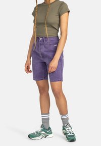 Lila jeansshorts i midjelång stil, med sidorfickor. Kombinerade med en åtsittande, olivgrön crop top. Grå strumpor och gröna sneakers.