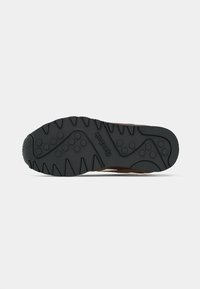 Crna gumena potplata Reebok tenisice koja prikazuje teksturirane uzorke za grip i kružne utore na neutralnoj pozadini.