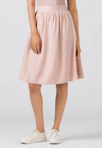 Ljusrosa, knälång kjol med rynkad midja och slät textur, kombinerad med vita sneakers. Enkel, avslappnad design.