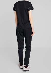 Zwart atletisch outfit met een top met korte mouwen en taps toelopende broek, gemaakt van rekbare stof. Voorzien van contrasterende witte accenten en spikes.