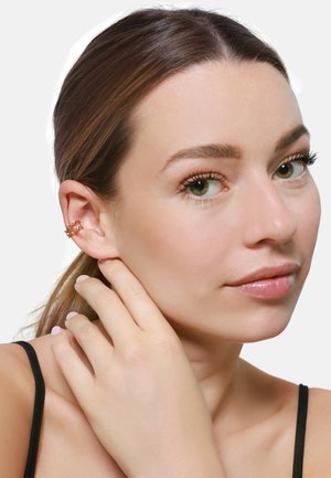 Gouden oorcuff met een gelaagd, open ontwerp en een gladde afwerking, gedragen aan het linkeroor. Het model heeft een lichte huid en schouderlang haar.