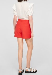 Rode geribde shorts met een soepele tailleband, gecombineerd met een lichtgekleurde top met rimpel mouwen. Zwart-witte sandaal schoeisel.