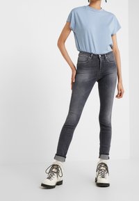 Jeans ajustados grises con una cintura de altura media, combinados con una camisa azul clara. Llevados con botas de cordones blancas y negras. Textura de tela suave.
