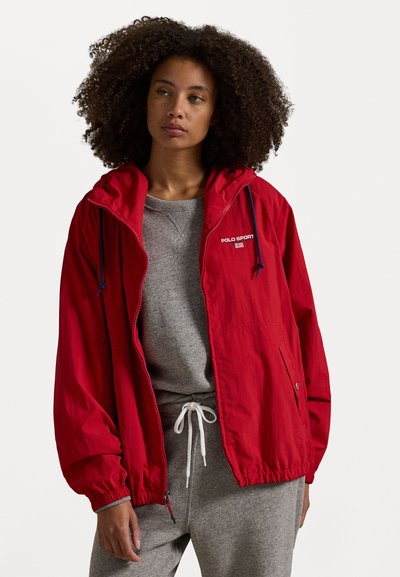 Κόκκινη αδιάβροχη ζακέτα με κουκούλα, ελαστικούς καρπούς και στρίμωγμα στο τελείωμα, που φιλοξενεί το λογότυπο "Polo Sport". Υφασμάτινη επιφάνεια και μπροστινές τσέπες.