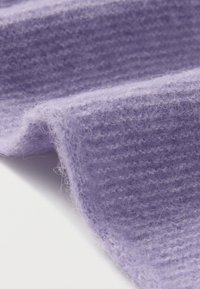 Lilla tekstureret stof med en blød, lodden overflade, der viser vævede mønstre og lette variationer i farvetonen. Kanterne er let frynset.