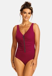 Bordowy jednoczęściowy kostium kąpielowy z dekoltem w kształcie V, przednim zamkiem błyskawicznym i marszczeniami w okolicy talii. Wykonany z gładkiego, elastycznego materiału.