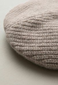 Lys beige strikket beret med et struktureret mønster og let glans, lavet af blød uld, med en afrundet, flad form.