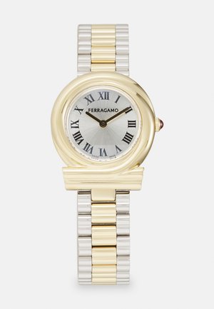 Gold and silver metal watch with a round case, Roman numerals, and a silver dial. Features a textured band and a decorative accent on the case.