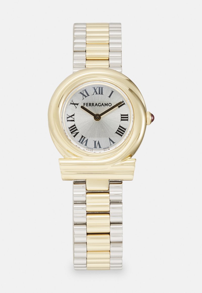 Kuld- ja hõbedavärvi metallkell, millel on ümmargune korpus, Rooma numbrid ja hõbedane kellapeegel. Omab tekstuuriga rihma ja dekoratiivset aktsenti korpusel.