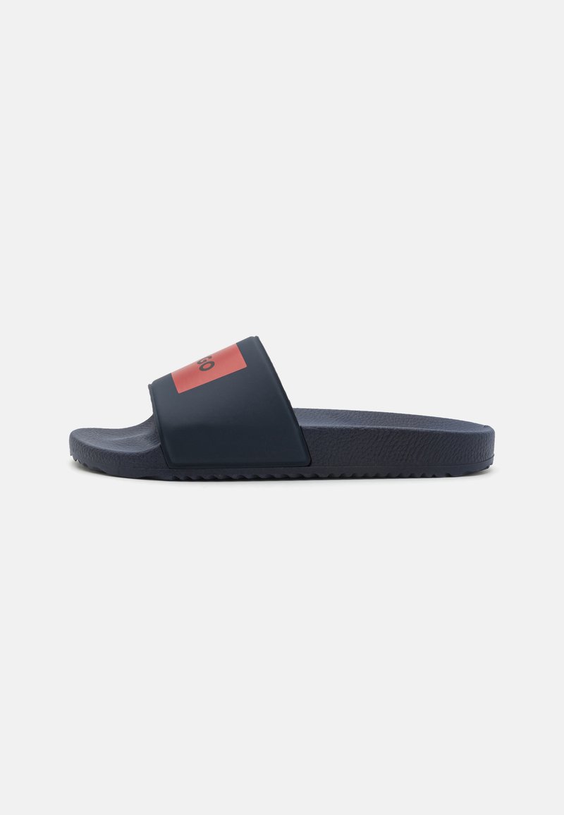 Marineblå slidesandal med teksturert såle, med en bred stropp i svart med rødt aksent og logo. Flat, uformell design som passer for utendørs bruk.
