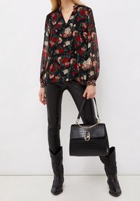 Blusa nera floreale con maniche lunghe trasparenti, abbinata a pantaloni di pelle nera e borsa in pelle di coccodrillo nera. Stivale da cowboy completa il look.