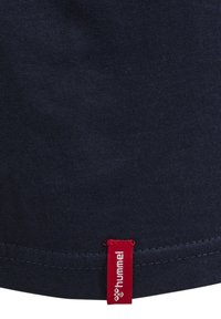 Marinblå bomull T-shirt som har en röd rektangulär etikett med texten "hummel". Tyget är slätt med en enkel yta och dubbelstickad fåll.