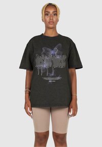 Schwarzes, übergroßes T-Shirt mit einem grafischen Design, das Schmetterlinge und stilisierte Schriftzüge zeigt. Kurze Ärmel, runder Halsausschnitt und lockere Passform.