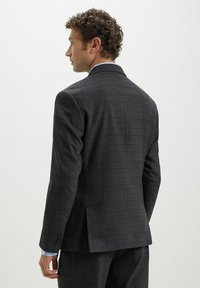 Blazer a quadri grigio carbone, design strutturato, chiusura a due bottoni, feritoie laterali, texture del tessuto visibile, abbinato a una camicia azzurro chiaro sotto.