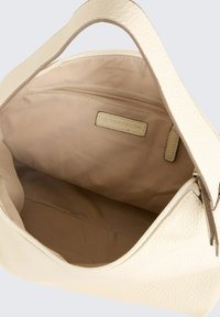 Crèmekleurige handtas met ritsluiting, voorzien van een beige interieur en een klein ritsvakje. Inclusief een debosserend merkembleem.