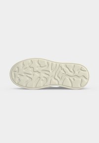 Semelle d'une chaussure beige clair avec des motifs de bandes de roulement ondulées et courbées irrégulières sur un fond blanc uni.