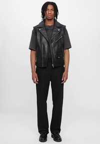 Zwarte leren motorvest met zilveren ritsen, gecombineerd met een donkergrijs shirt en zwarte broek. Gestyled met een strak, minimalistisch ontwerp.