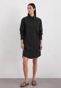 Zwarte blouse jurk met een kraag, lange mouwen en een rechte silhouet. Gemaakt van een zachte stof, met een licht gebogen zoom.