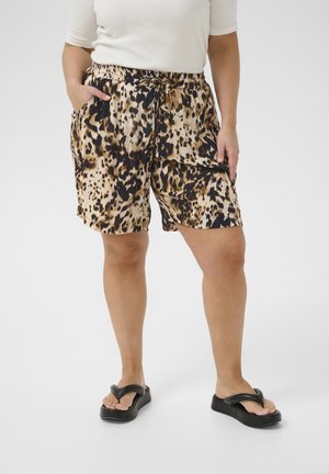 Pantaloni corti a stampa leopardo in beige, marrone e nero con vita elastica, dettaglio con lacci e tasche laterali. Indossati con sandali flip-flop neri.