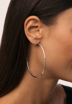 Orecchino a cerchio in argento con un design sottile e liscio. Grande forma circolare attaccata al lobo dell'orecchio, che riflette la luce con una finitura lucida.