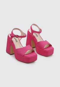Sandalias de plataforma rosas con parte superior de tela texturizada, diseño de punta abierta, tira en el tobillo y tacones gruesos. Acentuadas con un cierre de hebilla.