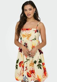 Robe d'été florale avec une base jaune, ornée de motifs rouges, orange et verts vifs, dotée de fines bretelles et d'un corsage ajusté menant à une jupe évasée.