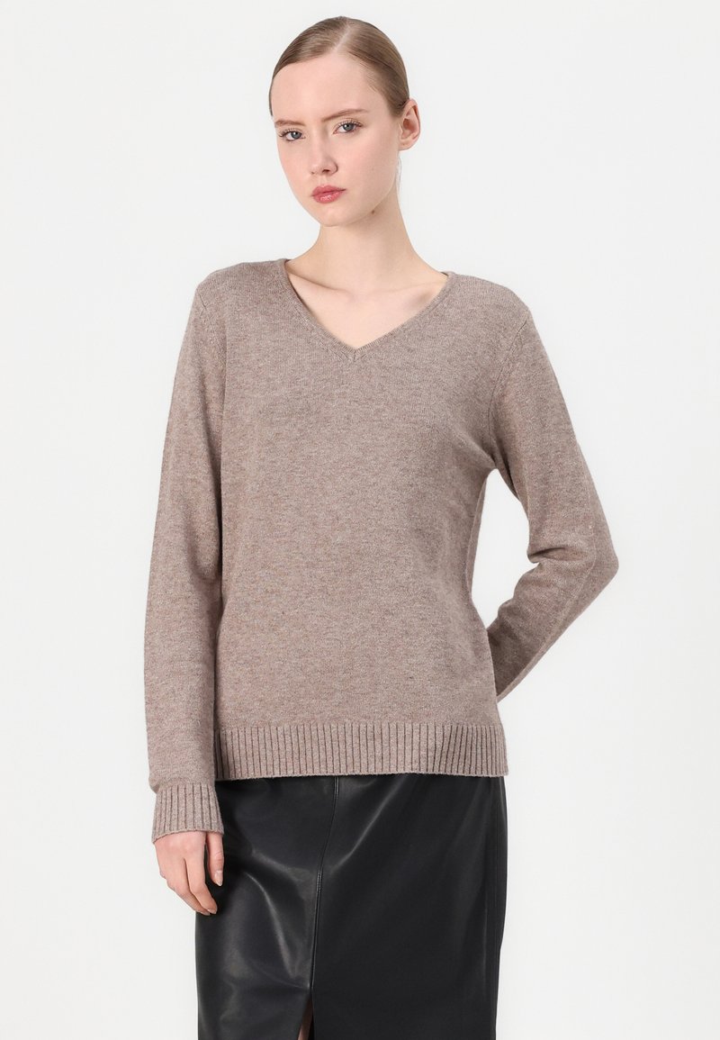 Pull en V couleur brun clair, fabriqué à partir d'un doux mélange de laine. Il présente des manches longues et des ourlets côtelés, associé à une jupe en cuir noire.