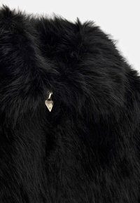 Melnā mākslīgā kažokādas audums ar gariem, mīkstiem šķiedrām. Iezīmējas ar zeltainu aksesuāru ar trīsstūrveida formu un pievienotām logotipiem.