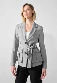 Blazer gris clair avec ceinture à la taille, deux poches avant et une silhouette ajustée. Le matériau semble lisse avec une texture subtile.
