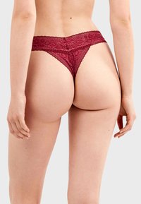 Tanga burdeos de encaje con una amplia cinturilla de estampado floral y cobertura mínima en la parte trasera, que resalta una textura delicada.