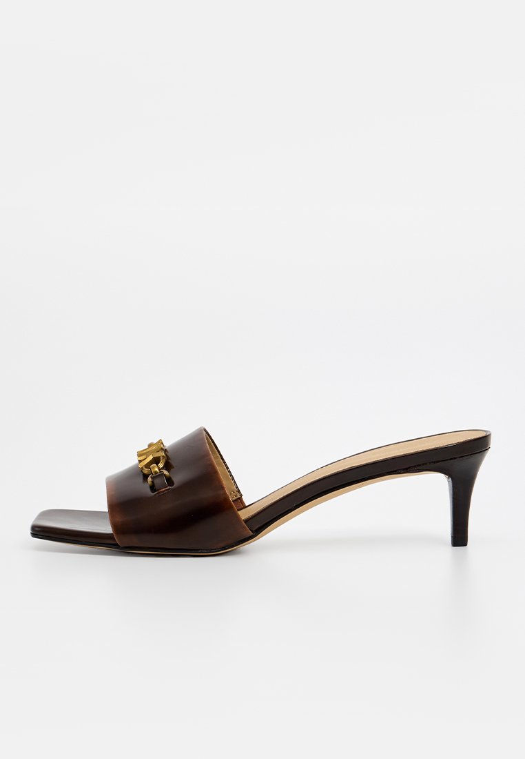 Brown leather slide sandal with a low heel, featuring a rounded toe and a gold accent detail on the strap. Smooth texture, minimalist design.