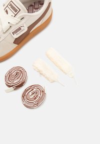 Tenisky Puma Palermo v off-white barvě s hnědými akcenty, s texturovaným svrškem a gumovou podrážkou, dodávány se dvěma párů tkaniček.