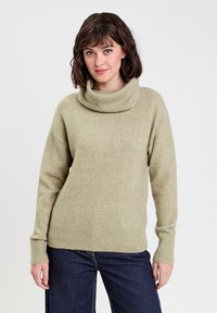 Pull à col roulé vert clair en tissu doux, avec des poignets et un ourlet côtelés, à coupe décontractée et épaules tombantes.