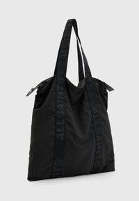 Black nylon tote bag with dual handles, featuring embossed branding along the straps, a soft texture, and a spacious design.
